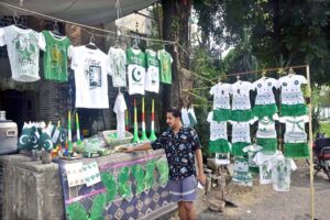 A vendor arranging and displaying national flags, shirts and dresses for children in connection with upcoming Independence Day celebrations at his roadside setup in Federal Capital