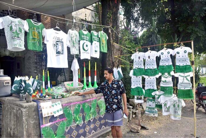 A vendor arranging and displaying national flags, shirts and dresses for children in connection with upcoming Independence Day celebrations at his roadside setup in Federal Capital