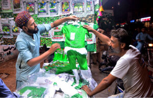 A man buys a child's outfit in national colors from a shopkeeper in Latifabad, with great excitement for Independence Day preparations