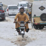 A motorcyclist passing through rainwater accumulated on the road after monsoon rain in the city