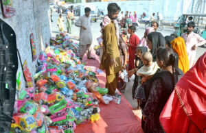 Women along with children are purchasing toys from a roadside vendor.
