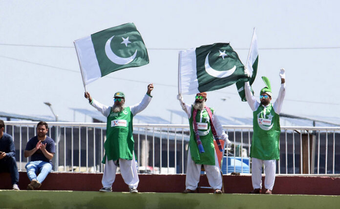 Supporters of Pakistan Cricket team wave national flags during the second day of the last cricket Test match between Pakistan and Bangladesh at Pindi Cricket Stadium