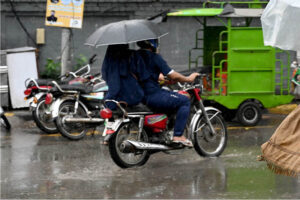 A woman holding an umbrella to protect from rain while sitting rear seat of motorcycle in the Provincial Capital.