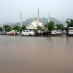 Female students wait for their college bus during a downpour in the Federal Capital