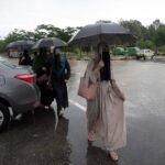 Women walk in front of Faisal Masjid, sheltered under umbrellas in the Federal Capital