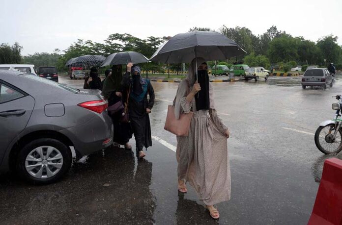 Women walk in front of Faisal Masjid, sheltered under umbrellas in the Federal Capital