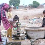 A woman and her children fill their pots with water from a hand pump at Norani Basti on the outskirts of the city