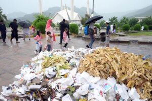 Women walk in front of Faisal Masjid, sheltered under umbrellas in the Federal Capital