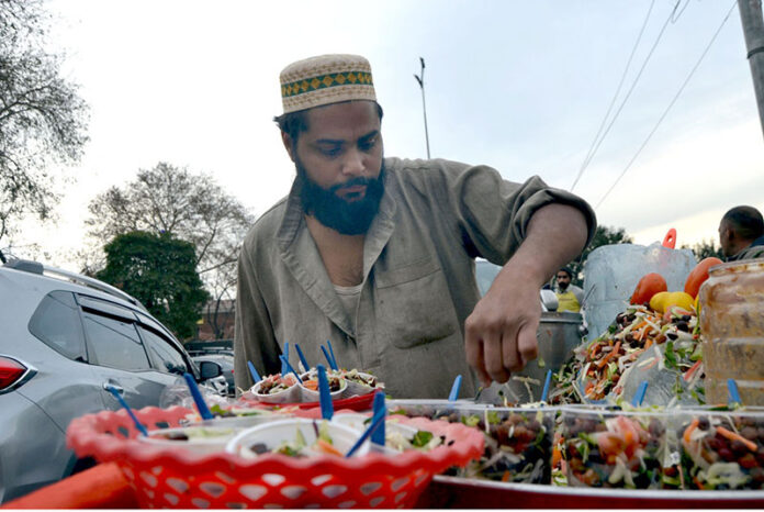 A street vendor draws the attention of customers near the railway station with a tray of zesty Alochana Chaat, enhanced with colors, spicy chili and sour flavors