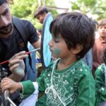 A boy making a design on a child face during celebrating Independence Day