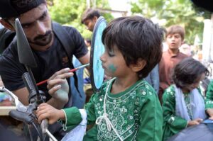 A boy making a design on a child face during celebrating Independence Day
