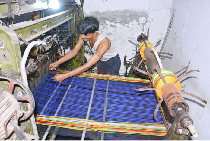 A worker is busy operating a power loom to prepare cloth in a local factory