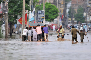 Youngsters lend a hand as they struggle to push a tricycle rickshaw through rainwater-flooded Hasan Parwana Road after a torrential downpour in the city
