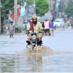 Youngsters lend a hand as they struggle to push a tricycle rickshaw through rainwater-flooded Hasan Parwana Road after a torrential downpour in the city