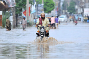 Youngsters lend a hand as they struggle to push a tricycle rickshaw through rainwater-flooded Hasan Parwana Road after a torrential downpour in the city