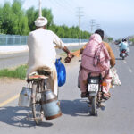 An elderly person on bicycle is holding the hand of a motorcyclist to reach his destination