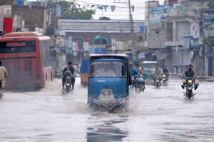 Youngsters lend a hand as they struggle to push a tricycle rickshaw through rainwater-flooded Hasan Parwana Road after a torrential downpour in the city