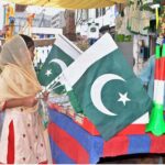 A young girl purchasing national flags from the roadside vendor in connection with upcoming Independence Day celebrations