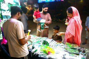 Family selecting and purchasing National flag and other items in connection with upcoming Independence Day celebrations from roadside stall at Latifabad.