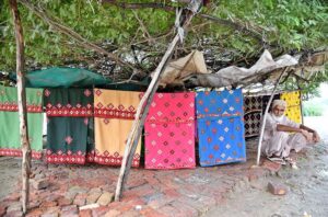 An aged man, displaying handmade bed sheets to attract the customers at Miro Khan Road.