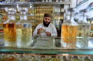 A vendor filling glass bottle with local perfume ‘ittar’ for the customer at Hashtnagri area