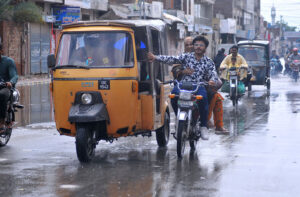 An out-of-order motorcycle rider holding onto an auto rickshaw's handle to reach his destination. during heavy rain in the city.