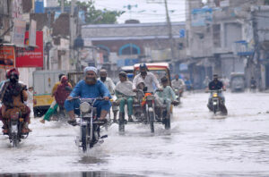 An out-of-order motorcycle rider holding onto an auto rickshaw's handle to reach his destination. during heavy rain in the city.