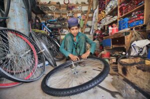A young mechanic busy repairing bicycle tyre at his workplace, Sikandar Pura.