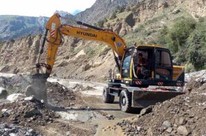 Worker busy in clearing blocked road with the help of heavy machinery after rain and land sliding in the area at Nalter Express Way.
