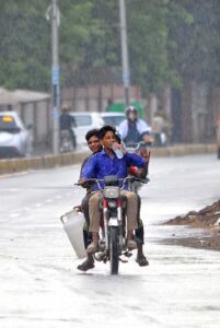 A young motorcyclist, drinking water while riding without a license plate during monsoon rain, is at high risk of causing an accident due to their disregard for traffic laws and unsafe behavio.