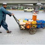 A man pushes a handcart loaded with water cans for sale in the market in front of Qilla Balasar