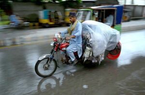 A motorcyclist on Saddar Road covers his luggage with plastic sheet to stay dry in the rain