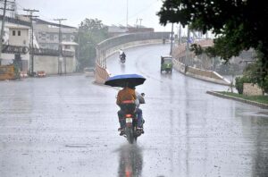 A young motorcyclist, drinking water while riding without a license plate during monsoon rain, is at high risk of causing an accident due to their disregard for traffic laws and unsafe behavio.