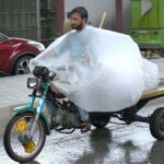 A motorcyclist on Saddar Road covers his luggage with plastic sheet to stay dry in the rain