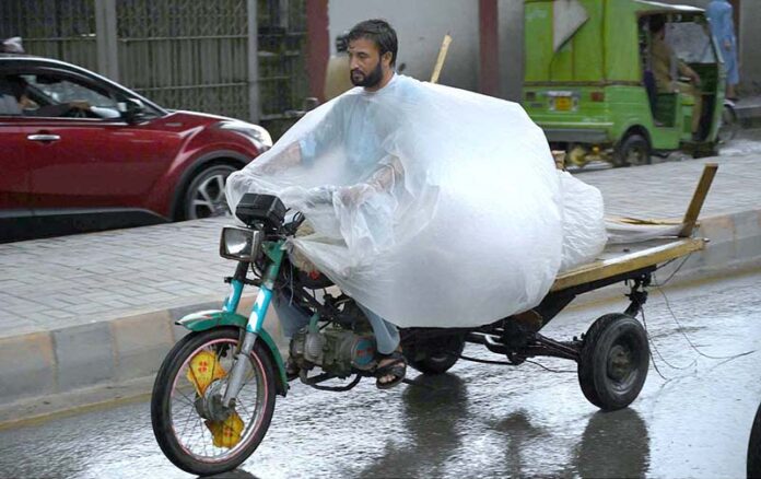 A motorcyclist on Saddar Road covers his luggage with plastic sheet to stay dry in the rain
