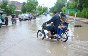 A motorcyclist navigate through flooded road accumulated rain water by torrential rain during Monson spell on the roads in Latifabad. .