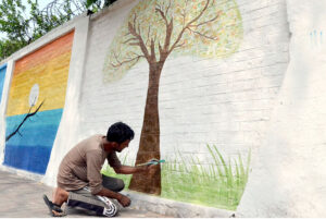 An artist painting a motivational wall mural on the Government Kinnaird High School wall to capturing the students' attention.