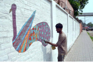 An artist painting a motivational wall mural on the Government Kinnaird High School wall to capturing the students' attention.