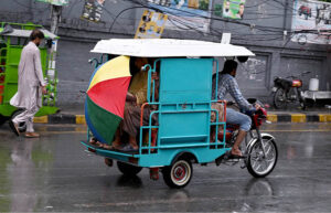 People sitting on a tricycle rickshaw cover themselves with an umbrella to stay dry during rain in the Provincial Capital.