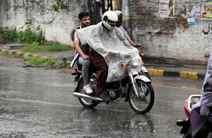 People sitting on a tricycle rickshaw cover themselves with an umbrella to stay dry during rain in the Provincial Capital.