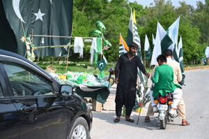 Commuters purchasing national flag displayed by the roadside vendors as the nation celebrates the Independence Day of Pakistan