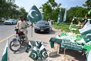 Commuters purchasing national flag displayed by the roadside vendors as the nation celebrates the Independence Day of Pakistan