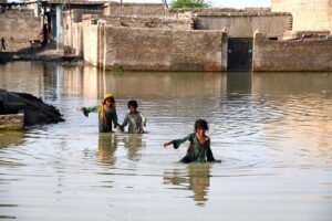 Children crossing flooded streets where rainwater has accumulated in front of houses at Qutb Colony