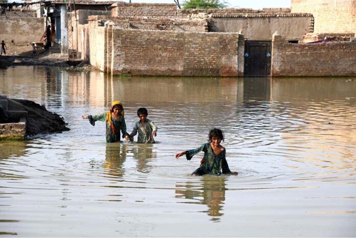 Children crossing flooded streets where rainwater has accumulated in front of houses at Qutb Colony