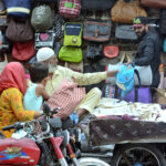A motorcyclist selecting school bag for his kids from a roadside vendor