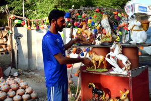 A vendor arranging and displaying the different kinds of clay made decoration items to attract the customers at his roadside setup
