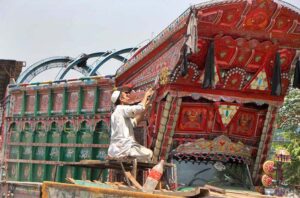 An artist on a ring road decorates a truck with intricate designs, a hallmark of expensive truck art in Pakistan.