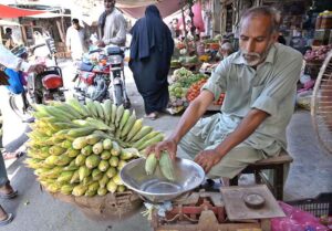 A vendor is selling corn to a customer at his roadside setup at urdu bazaar.