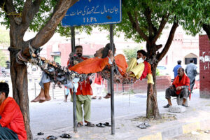 Railway Coolies (porters) chatting while resting on a swing and waiting for clients outside Lahore Railway Station.