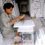 A skilled worker carves intricate names into a piece of marble at his workplace